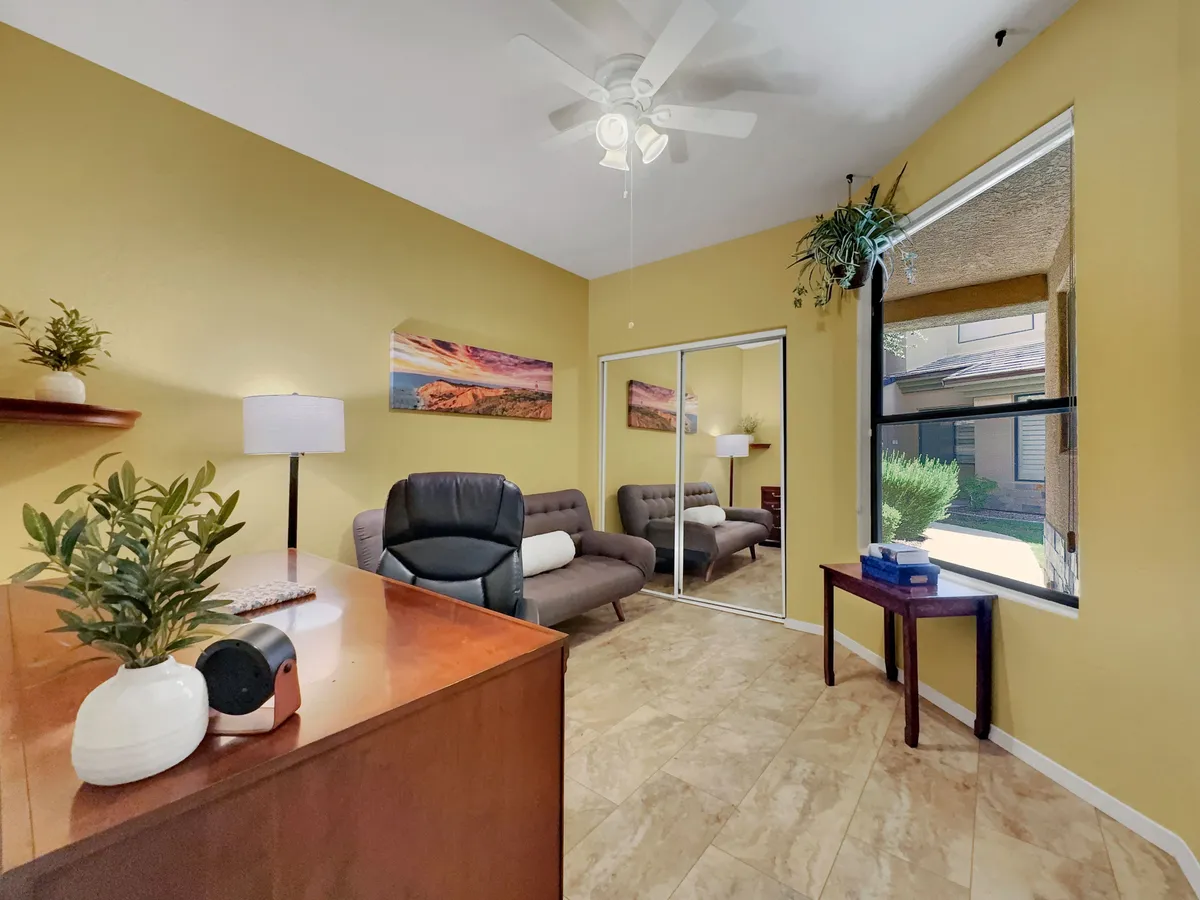 A multi-functional area combining a desk with a chair for workspace needs, plush sofas for lounging, decorative wall art, a potted plant, and a window that lets in natural light. The layout is tailored for professionals and families alike, offering options for work and relaxation.
