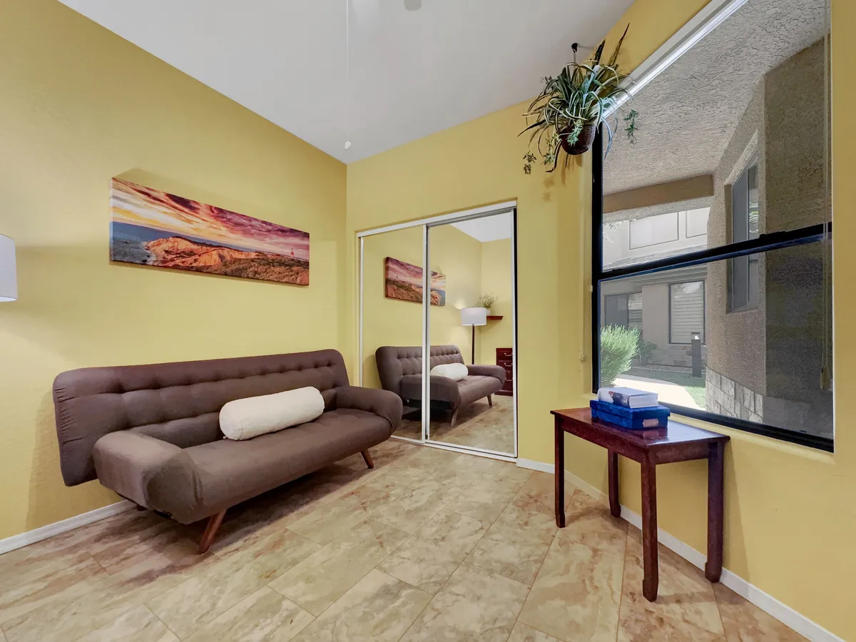 A sunlit living room with a comfortable sofa, decorative artwork, a side table, and a large window that connects the interior space to the outdoors. The natural light and spaciousness suggest relaxation after a day out.