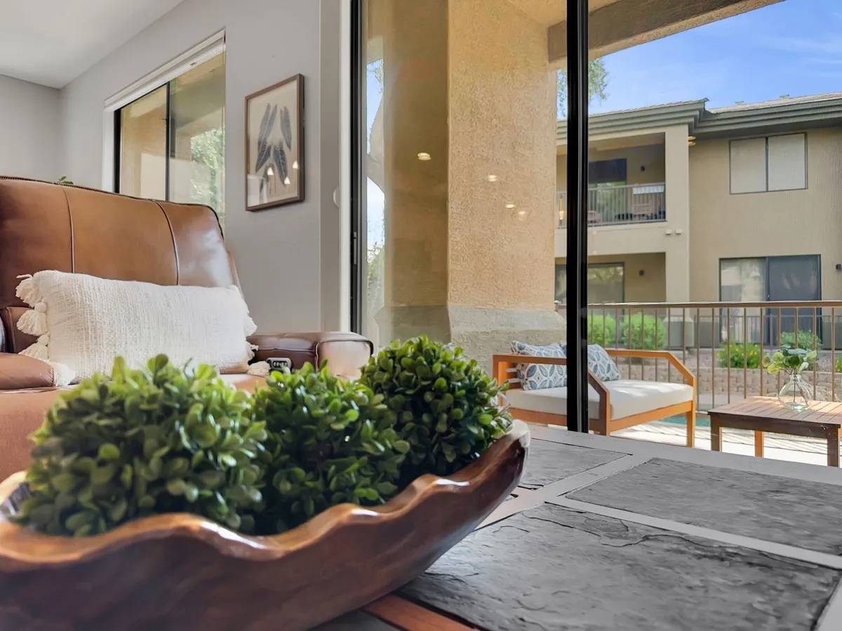 A bright and comfortable living room with a leather sofa, a decorative bowl filled with greenery on the coffee table, and large glass doors opening to the outside. Sunlight pours in, connecting the interior space with the outdoors and highlighting the seamless flow between indoor and outdoor living.
