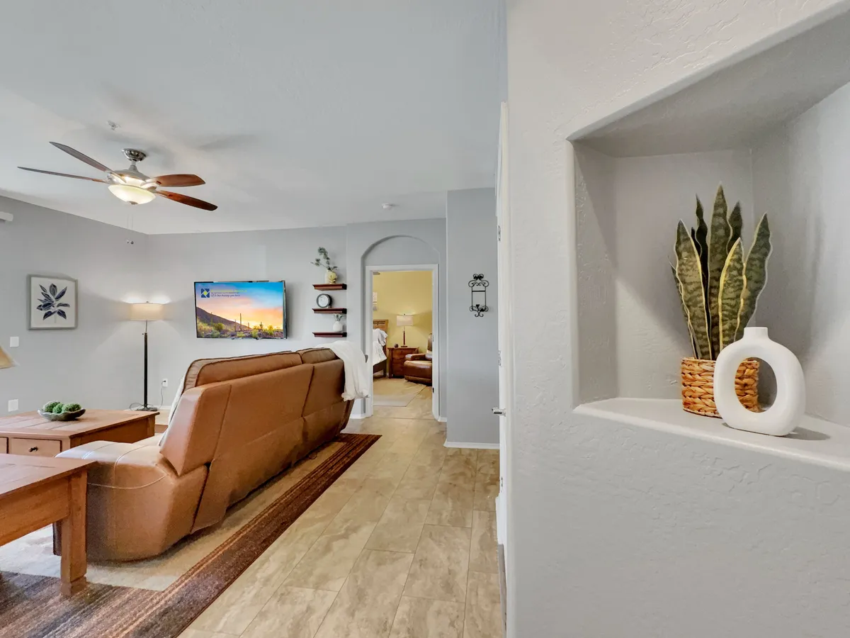 A stylish living room setup with a leather sofa, an inviting coffee table, modern wall art, a TV, and green plants nestled into a wall niche. The setup offers multiple seating options and is well-suited for both entertainment and quiet relaxation.