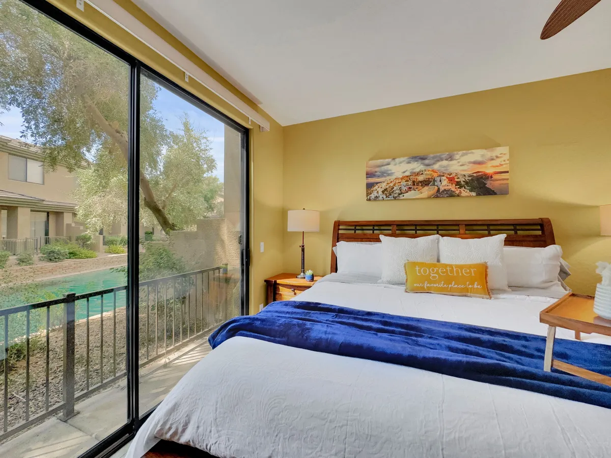A spacious bedroom with a large window offering a scenic view, a neatly made bed with decorative pillows, and a nightstand with a lamp. The room exudes a cozy and serene atmosphere, perfect for relaxation at the end of the day.