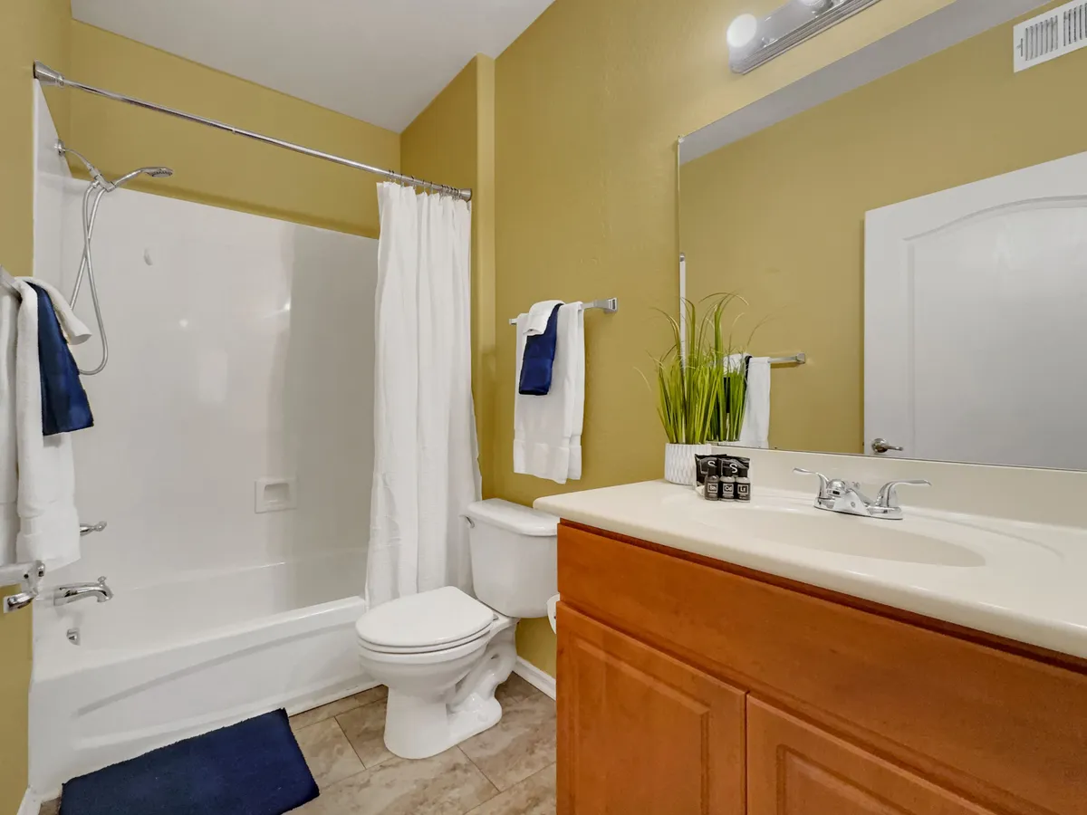 A modern bathroom with a sleek vanity and sink, a mirrored wall, a decorative plant, and a walk-in shower area. The space is organized and calm, ideal for daily grooming and relaxation.