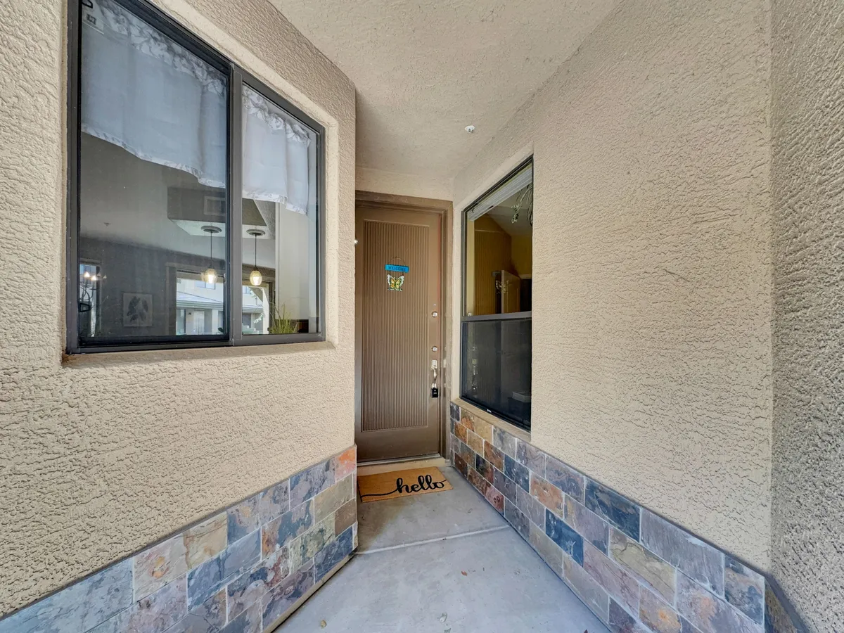 This image showcases the front door of the condo, framed with a welcome mat and windows that allow natural light to filter in. The entryway gives a sense of arrival and hospitality, offering a glimpse of the home's inviting nature.