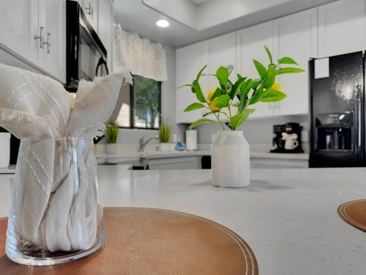 A close-up view of the kitchen's countertop area, featuring a detailed napkin arrangement, a potted plant, and visible countertop materials alongside kitchen appliances. The arrangement suggests an environment ready for cooking and entertaining, emphasizing both function and style.