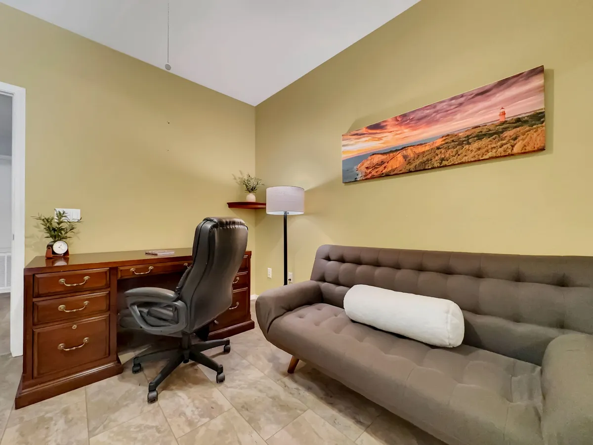 An interior view of a work-friendly space featuring a wooden desk with a comfortable chair, a modern sofa, and wall art. The mood is cozy yet productive, emphasizing the condo’s suitability for remote work or quiet focus.